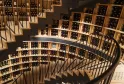 Spiral wine cellar with wooden shelves holding hundreds of wine bottles, black metal staircase winding through the space, in Bordeaux.