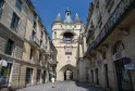 The Grosse Cloche of Bordeaux, a 13th-century medieval tower with three conical turrets, framed by historic buildings on a paved street in the old town.