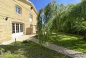 Stone house facade with paved terrace, white French doors and weeping willow in a sunny green garden