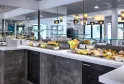 Modern breakfast buffet with black and white counter, fresh fruits, pastries and beverages in a bright room with mirrors and designer lighting at Hôtel Au Comté d'Ornon in Bordeaux.