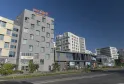 View of the Mer & Golf City Bordeaux Lac apart-hotel featuring modern multi-story buildings in grey and white tones, located in the Lake district of Bordeaux, under a clear sky.