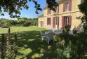 La Gontrie Castle in Bordeaux featuring a yellow stone facade with pink shutters, green lawn with white chairs and flowering gardens