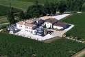 Aerial view of Château La Rose Perrière near Bordeaux, featuring modern white renovated buildings surrounded by vineyards and a river.
