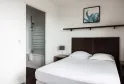 Modern bedroom with double bed with white linens, black headboard, adjoining bathroom with glass shower, minimalist décor and botanical artwork.