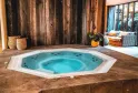 Indoor spa featuring a turquoise hot tub with massage jets, surrounded by rustic wooden walls, woven baskets, and warm-toned relaxation furniture.