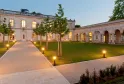 Illuminated courtyard of Table de La Chèze in Bordeaux, featuring stone buildings, manicured lawn, paved walkways and evening ambient lighting