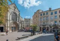 Sunny square in Bordeaux featuring the Saint-Pierre Church with its ornate Gothic facade and clock, surrounded by Haussmann-style stone buildings, with visitors and café terraces.