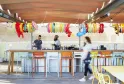 Modern bar at Mama Shelter in Bordeaux featuring wooden counter, colorful bar stools, staff members working, and festive hanging bracelet decorations on the ceiling.