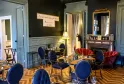 Elegant room at Cercle de Montaigne in Bordeaux featuring blue and red chairs, black tables, herringbone flooring, marble fireplace, gilded mirror, and framed French quote on dark wall.