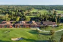 Aerial view of a luxury hotel complex with red-orange facades and brown roofs, surrounded by a lush golf course with bunkers, water features, and forests near Bordeaux.