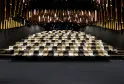 Interior of the Thomas Jefferson Auditorium at La Cité du Vin in Bordeaux, featuring tiered seating in beige and black tones, with an illuminated ceiling featuring golden and white light panels.