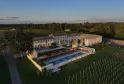 Aerial view of Château Fage, a luxury hotel-restaurant with ochre stone buildings, blue swimming pool, red loungers on terrace, surrounded by vineyards and forests in the Bordeaux region.