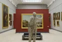 Gallery of the Bordeaux Museum of Fine Arts featuring a marble statue in the foreground facing gilt-framed historical paintings on white and burgundy walls, with overhead lighting.