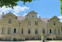 Front view of Château Maucaillou in Bordeaux, a grand pale yellow stone mansion with red tile roof, symmetrical pavilions, set on manicured lawn with garden furniture in the foreground.