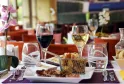 Elegant dining table set with red and white wine glasses, charcuterie plate, toasted bread basket, pink flower in vase, and cutlery on purple tablecloth in an upscale restaurant dining room.