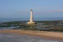 Cordouan lighthouse, a white and beige lighthouse with a red dome, standing on a rocky reef covered with seaweed off the coast of Bordeaux, surrounded by sandy beaches and the Atlantic Ocean.