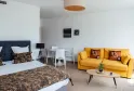 Spacious studio apartment with double bed, yellow sofa, white dining area and golden circular ceiling light at Ténéo Apparthôtel