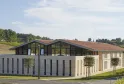 Château Peby Faugères in Bordeaux: modern architectural building with white and grey facades, red tile roof, large glass panels and black shutters, surrounded by landscaped gardens and vineyards.