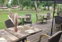 Outdoor dining terrace at Bistrot du Lac in Bordeaux featuring set tables, wicker chairs, black umbrella, floral decorations and a view of a green park with trees and small cottages in the background