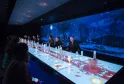 Futuristic dining room with interactive illuminated table, panoramic nighttime view with moon and trees on giant screen, diners seated on both sides