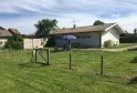 Exterior view of a rural cottage with a family under an umbrella in a fenced garden, in the Bordeaux region