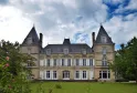 Front facade of the National Health Insurance Museum in Bordeaux, a Second Empire-style château with two pointed towers, surrounded by green lawns and pink flowers.