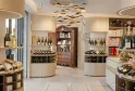 Elegant interior of a wine shop in Bordeaux featuring wine bottle displays on light wood and white shelving, a golden chandelier pendant light, and a vintage wooden cabinet in the center.