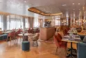 Elegant restaurant at Madame B in Bordeaux featuring red chairs, round tables, glossy white ceiling, large bay windows, and light wood modern furniture
