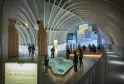 Interior of the Cité du Vin in Bordeaux featuring a modern arched white ceiling design, visitors viewing an illuminated scale model of the Bordeaux vineyard, and exhibition screens on the walls.