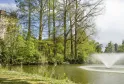 View of Bourran Park in Bordeaux featuring a historic stone tower, a lake with fountain, majestic trees and lush spring vegetation.