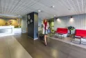 Modern lobby of Ténéo Apparthotel Bordeaux-Mérignac featuring white reception desk, wall clocks, red sofas and moving guests