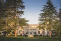 Classical white facade of Château Haut-Bailly in Bordeaux, surrounded by majestic cedar trees under clear sky.