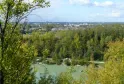 Panoramic view of Parc de l'Ermitage Sainte-Catherine in Bordeaux featuring a lake in the foreground, poplar forest, and city skyline under a cloudy sky