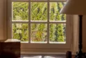 View from a mullioned window of a desk overlooking organized vineyard rows in Bordeaux, with a red armchair in the foreground and golden vines under sunlight.