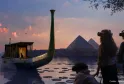 Fantastical view of an illuminated traditional boat on water at sunset, with Egyptian pyramids in the background and visitors watching the scene from the shore in Bordeaux.