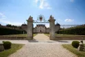 Overview of Château de Malle in Bordeaux, featuring ornate stone gateways with sculptures, wrought iron fencing, gravel drive, and a classical mansion with mansard roof.