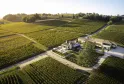 Aerial view of Château de Candale near Bordeaux, surrounded by neatly arranged vineyard rows with residential buildings and an irrigation canal winding through the cultivated landscape.