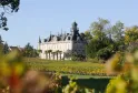 Marquis d'Alesme Becker Castle, a grand Bordeaux-style château with towers and mansard roof, surrounded by autumn vineyards in the Bordeaux wine region.