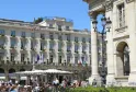 The Intercontinental Grand Hotel Bordeaux facade featuring its lively outdoor terrace, ornate balconies, Corinthian columns and flags under clear blue sky.