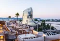 Panoramic terrace of Renaissance Bordeaux Hotel featuring contemporary furniture, overlooking the Garonne River and modern glass and steel building architecture at dusk