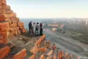 Four people standing on a red rocky cliff overlooking the panoramic view of Bordeaux city, river, and buildings in golden light.