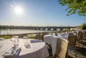 Restaurant terrace overlooking the Garonne River in Bordeaux with set tables, view of the Stone Bridge and city skyline on a sunny day