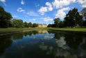 Château La Louvière near Bordeaux, a classical stone mansion with ochre-colored facade centered in a large manicured lawn, reflected in a canal with mature trees framing the estate under a clear blue sky.