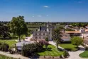Aerial view of Château Pape Clément in Bordeaux, a white neo-gothic castle surrounded by formal gardens and vineyards, under a clear blue sky.