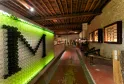 Interior of the Museum of Wine and Vine Crafts in Bordeaux, featuring an artistic installation of illuminated green and black bottles forming a graphic pattern on the left wall, with a terracotta exhibition corridor, display cases, and wooden ceiling beam