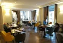 Elegant dining room at Comptoir de Sèze in Bordeaux featuring black tables, yellow and blue chairs, large windows, beige and gold decor, with an outdoor terrace view.