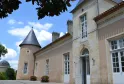 Facade of Château Lescombes, a contemporary art center in Bordeaux, featuring its distinctive round tower, white windows, and beige stone walls under a blue sky.
