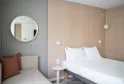 Modern hotel room at Novotel Bordeaux Mérignac featuring a double bed with white linens, minimalist furnishings, round mirror, and beige and grey tones.