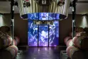 Modern winery facility at Château La Fleur de Boüard in Bordeaux, featuring oak barrels on either side and a large digital screen displaying an illuminated grape cluster pattern in blue and purple.