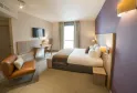 Modern hotel room featuring a double bed, cognac leather armchair, desk, wall-mounted television and large windows overlooking Bordeaux